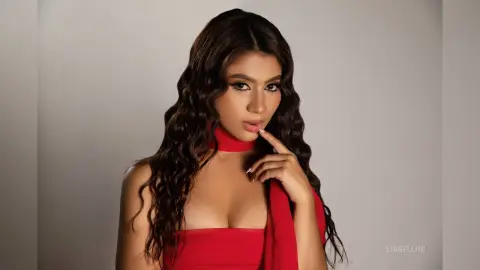 Glamorous woman with long wavy hair wearing a chic red halter dress in a studio setting.