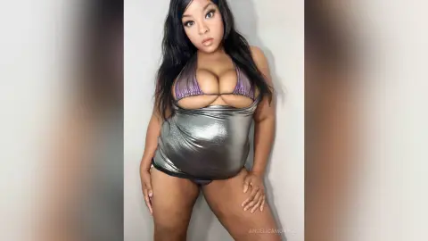 Curvy woman in a metallic silver mini dress posing against a white wall for a glamorous studio portrait.