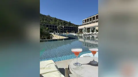 Refreshing pink cocktails on a table overlooking a luxury resort swimming pool on a sunny summer day.