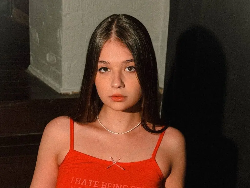 Young woman in a red graphic camisole tank top posing in moody, low-light indoor setting.