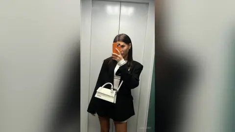 JadaJosey takes a mirror selfie in a black blazer and white top while holding an orange phone.