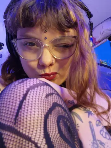 Woman with glasses and nose ring wearing a mesh top in moody blue lighting.