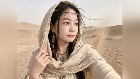 CelesteQi — CelesteQi wears a beige headscarf and ornate jewelry while posing in a vast desert landscape.