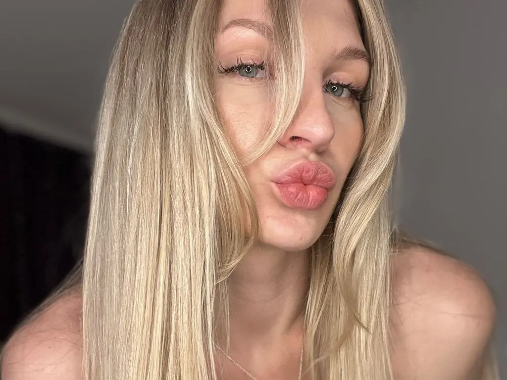 Blonde woman with long hair making a playful pouty face in a casual indoor setting.