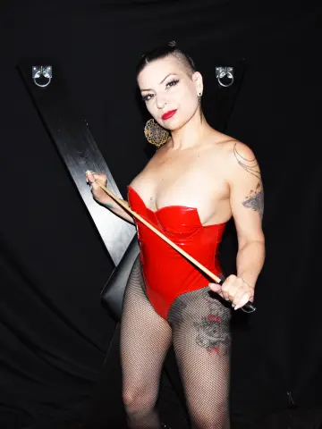 Glamorous woman in a red corset and fishnet tights posing against a black backdrop with bold red lipstick.