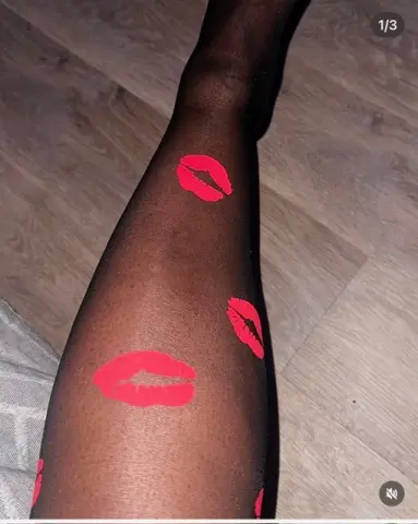 VeraMonae — Close-up of a person's leg wearing sheer black tights decorated with bright red lipstick kiss prints.