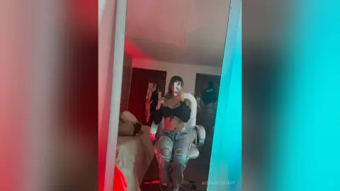 Young woman in a black crop top and ripped jeans taking a selfie in a moody, neon-lit bedroom.