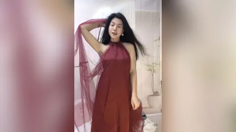 KireliaYan — KireliaYan poses in a flowing maroon halter dress while holding the sheer fabric up near her head.