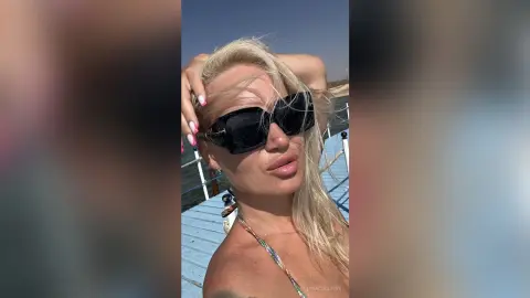 Blonde woman in black sunglasses enjoying a sunny summer day on a wooden pier by the ocean.