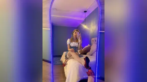 Woman in white corset and patterned skirt taking a mirror selfie in a moody, blue-lit bedroom.