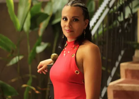 Smiling woman in a red sleeveless dress posing in a lush tropical garden setting.