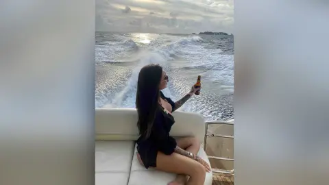Woman in black outfit relaxing on a boat deck with a drink during a sunset ocean cruise.