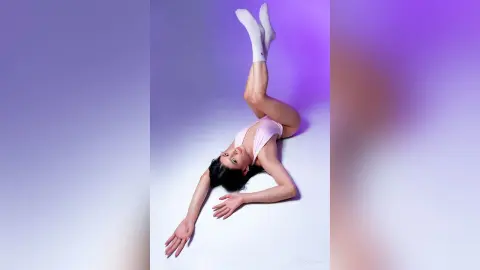 Graceful ballerina in a pink leotard performing a graceful pose against a soft purple studio background.