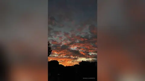 Dramatic orange and pink sunset clouds over a dark city skyline at dusk.