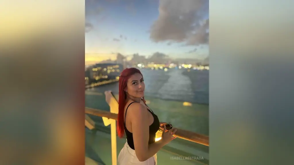 IsabellaEstrada with red hair poses in black lace lingerie and stockings while leaning over a wooden dresser.