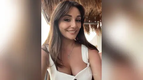 Smiling brunette woman in a white summer top relaxing under a thatched tropical sunshade.