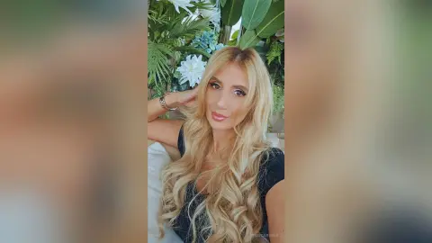 Smiling blonde woman in a black top relaxing in a lush tropical garden setting.