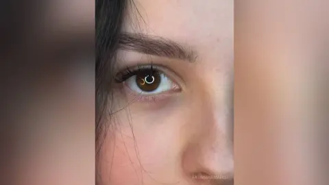 Close-up portrait of a young woman with dark hair and expressive brown eyes looking into the camera.