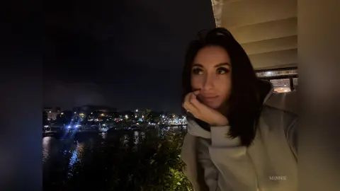 Thoughtful woman in a white hoodie relaxing by a city waterfront at night.