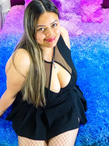 Smiling woman in a black cutout dress and fishnet tights sitting on a vibrant blue shag rug.