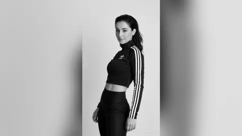 Woman in black Adidas tracksuit posing confidently against a minimalist studio background.