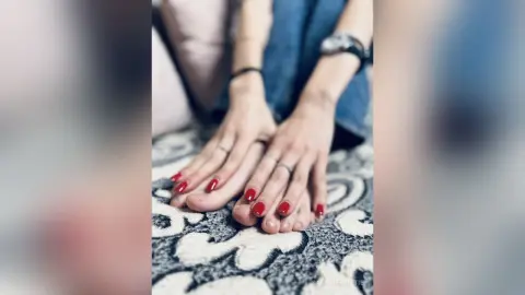 Close-up of a woman's feet with bright red nail polish resting on a patterned rug in a cozy indoor setting.