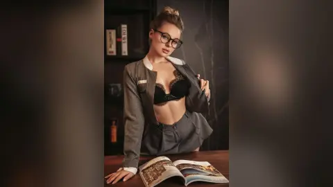 BeaNix wears black lace bra and a grey skirt suit while sitting behind an open book.