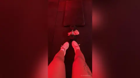 Person in white sneakers sitting on a gym floor under moody red lighting.