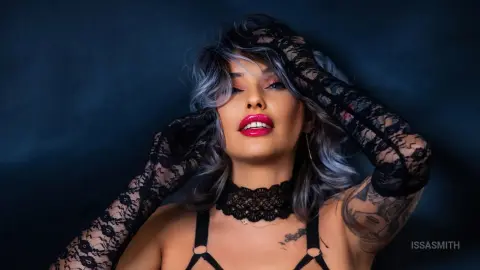 Glamorous woman with silver hair and black lace gloves posing against a dark blue background.