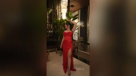 Elegant woman in a red evening gown posing in a luxurious modern hotel lobby with warm lighting.