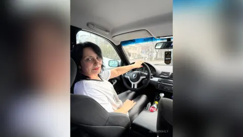 JesicaMaily — JesicaMaily sits in the driver's seat of a car wearing a white t-shirt and looking at the camera.