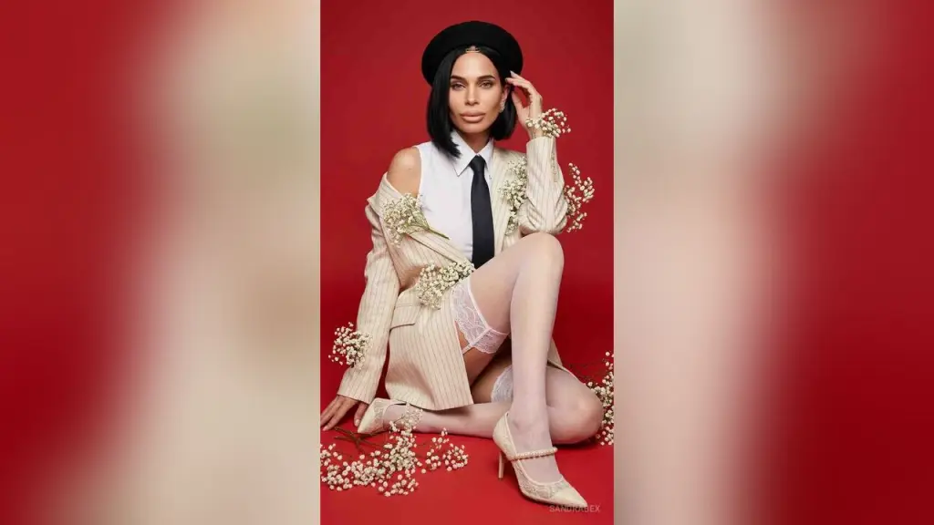 SandraBex — Elegant woman in a white shirt, black tie, and beige blazer adorned with flowers against a red background.