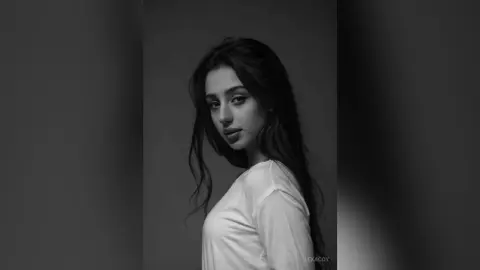 Moody black and white portrait of a young woman with long dark hair wearing a white t-shirt against a gray background.