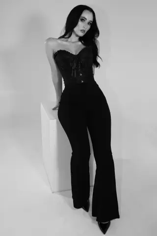 Elegant woman in black strapless jumpsuit posing against a white studio background in a moody black and white portrait.