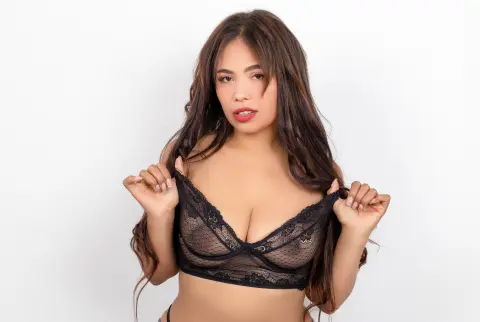 Young woman with long wavy hair wearing black lace lingerie against a white background.