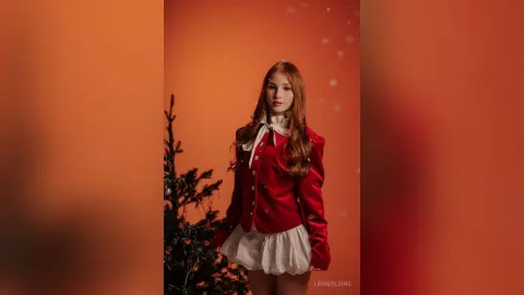 Elegant woman in a red velvet blazer and white skirt posing against an orange background with festive lighting.