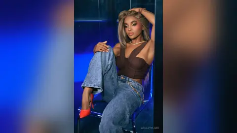 Stylish woman in a brown corset top and blue jeans posing confidently in a moody blue studio setting.