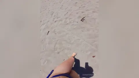 Close-up of a woman's legs relaxing on a sunny sandy beach in a blue bikini.