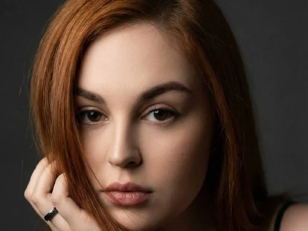 Close-up portrait of a woman with red hair and a thoughtful expression against a dark studio background.