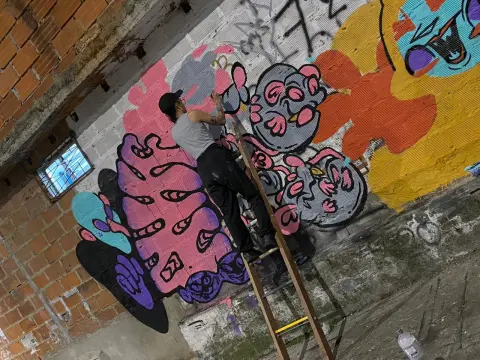 Artist in casual clothes painting colorful street art graffiti on a concrete wall using a wooden ladder.