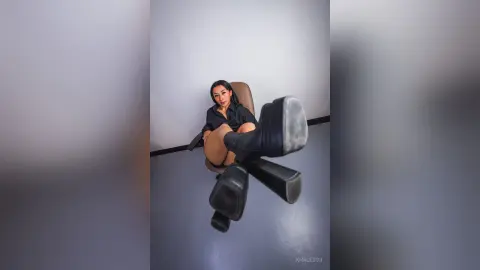 Stylish woman in a black shirt and boots sitting on a chair in a minimalist modern room.