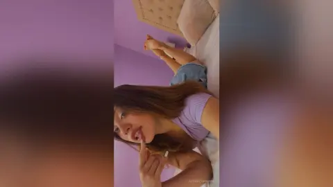 Young woman in a lavender ribbed top relaxing on a bed in a purple room with a dreamy mood.