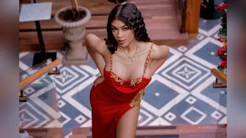 Glamorous woman in a red evening gown posing on a patterned staircase in a luxury setting.