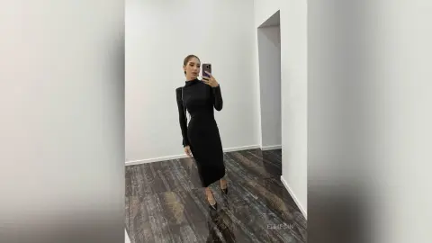 Elegant woman in a sleek black long-sleeve midi dress taking a mirror selfie in a modern minimalist room.