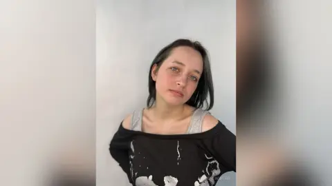 SoleneWinter looks at the camera with her dark hair down, wearing a black t-shirt with a white pattern that hangs off one shoulder.