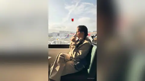 Stylish woman in beige loungewear sipping coffee by an airplane window on a bright morning flight.