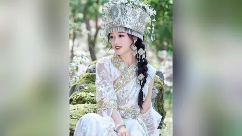 Elegant woman in ornate white traditional Chinese hanfu and silver crown posing in a lush green garden.