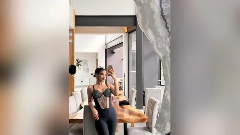 Woman in black lace bodysuit and leggings standing in a bright modern minimalist dining room.