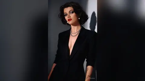 Elegant woman in a black blazer and silver chain necklace posing with moody studio lighting.