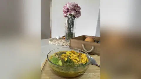 A bowl of steaming yellow curry soup served on a wooden tray in a bright, cozy kitchen setting.